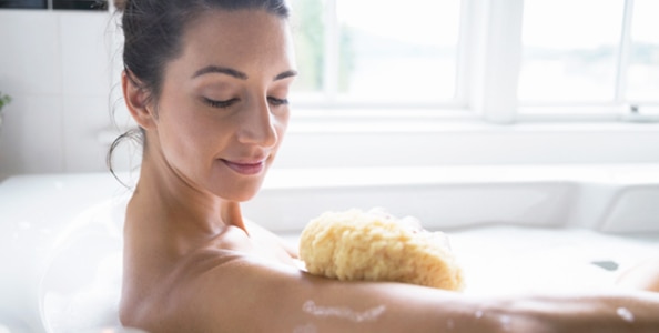 Chica bañandose y usando esponja para cuidar su piel